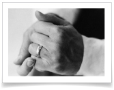A close up photo of the hands of a married couple wearing wedding bands.