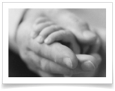 A caregiver holds the hand of a sick infant.