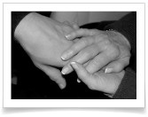 A caregiver lovingly holds the hand of a terminal patient in a Raleigh hospice house.